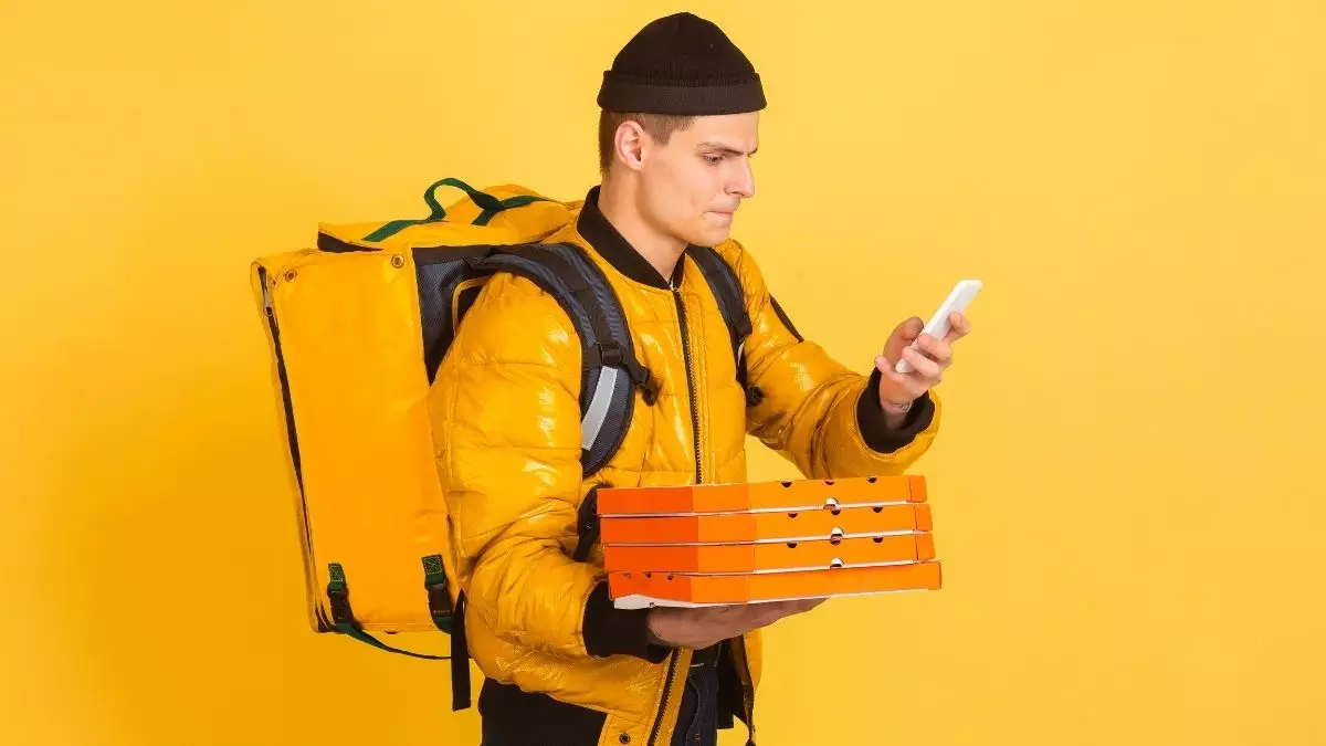 Homem com mochila de entregas, segurando pizzas e olhando celular - Startups