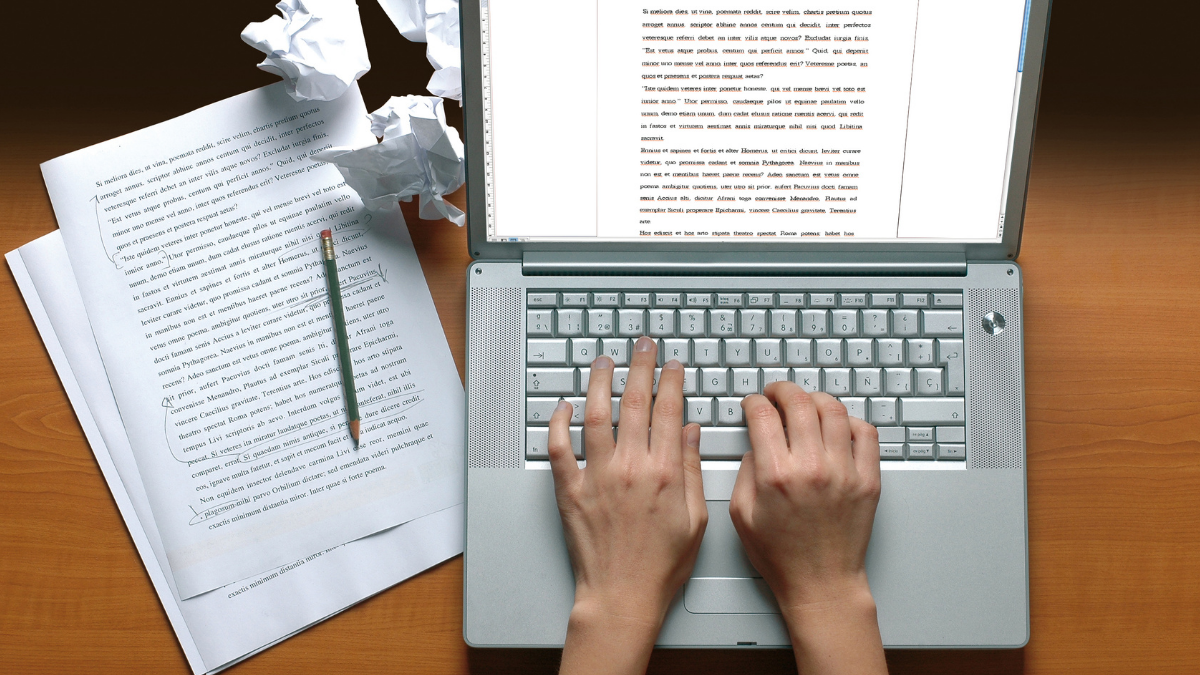 Duas mãos digitando em um teclado de notebook com rascunhos e alguns papéis amassados ao lado - Startups