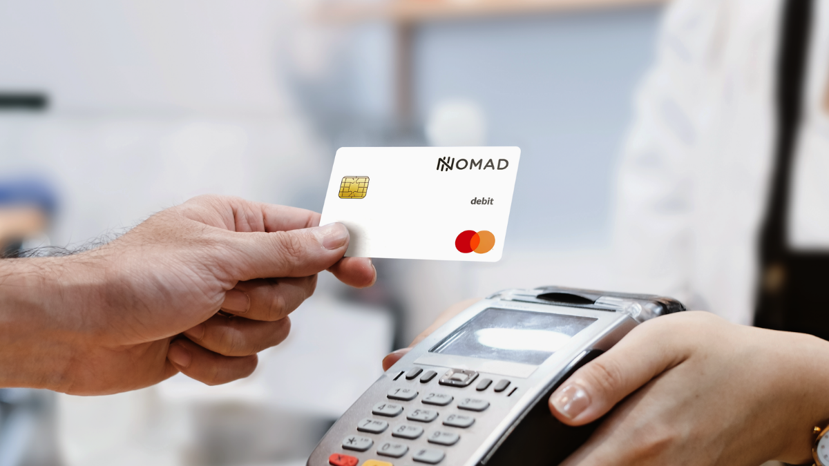 Uma mão segurando o cartão do banco Nomad e uma outra mão segurando a máquina de recebimento de cartões - Startups